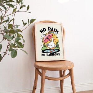 May include: A framed print with a white background and a cartoon illustration of a goose holding an umbrella. The text "NO RAIN NO RAINBOWS" is printed in black below the goose.