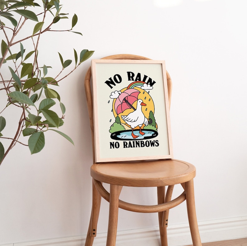 May include: A framed print with a white background and a cartoon illustration of a goose holding an umbrella. The text "NO RAIN NO RAINBOWS" is printed in black below the goose.