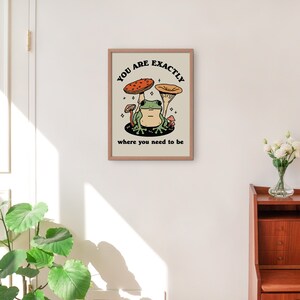May include: A framed print with a beige background featuring a green frog sitting on a mushroom with the text "You are exactly where you need to be".