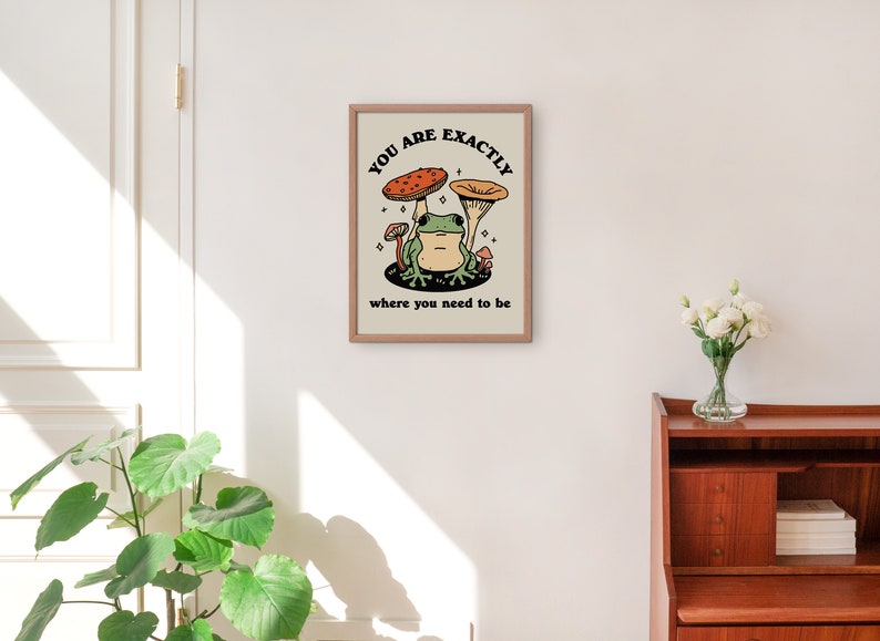 May include: A framed print with a beige background featuring a green frog sitting on a mushroom with the text "You are exactly where you need to be".