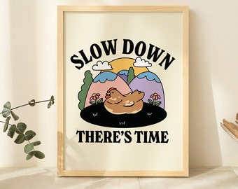 May include: A framed print with a white background and black text that reads "Slow Down There's Time". The illustration features a cartoon chicken in a field with mountains and a sun in the background.