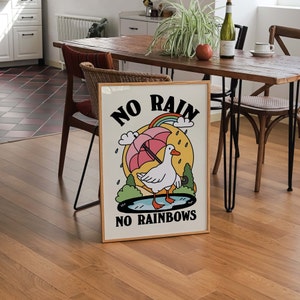 May include: A framed poster with a white duck standing in a puddle of water. The poster has a yellow background with the text "NO RAIN NO RAINBOWS" and a rainbow above the duck.