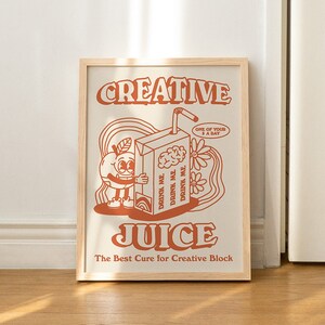 May include: A framed print with a retro-style illustration of a cartoon orange holding a juice box. The text on the print reads "CREATIVE JUICE The Best Cure for Creative Block".