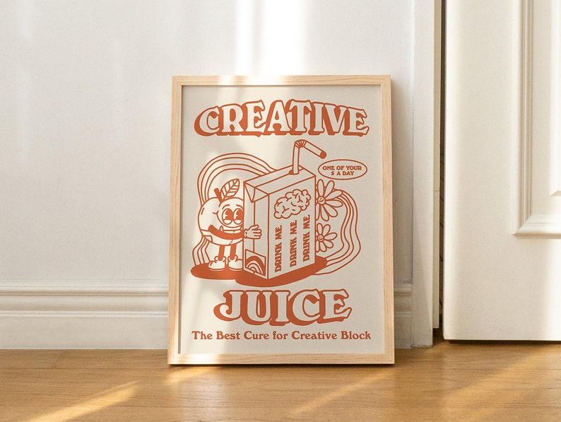 May include: A framed print with a retro-style illustration of a cartoon orange holding a juice box. The text on the print reads "CREATIVE JUICE The Best Cure for Creative Block".