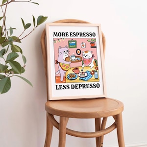 May include: A framed print with a pink background featuring two cartoon cats. The cat on the left is serving a cup of coffee to the cat on the right. The text on the print reads "More Espresso Less Depresso".