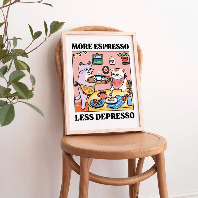 May include: A framed print with a pink background featuring two cartoon cats. The cat on the left is serving a cup of coffee to the cat on the right. The text on the print reads "More Espresso Less Depresso".