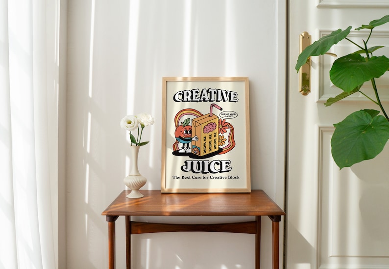 May include: A framed print with a cartoon illustration of a juice box with a face and the text "Creative Juice. The Best Cure for Creative Block." The juice box is holding a brain and has a thought bubble that says "I'm making the world a better place, one sip at a time."