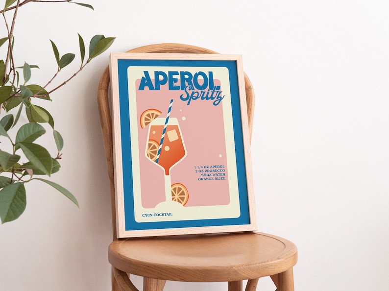 May include: A vintage-style poster with a pink background and blue border. The poster features a glass of Aperol Spritz with orange slices and a straw. The text on the poster reads "Aperol Spritz" and includes the ingredients: 1 1/4 oz Aperol, 3 oz Prosecco, Soda Water, Orange Slice. The poster also includes the text "CYUN COCKTAIL."