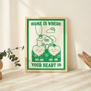 May include: A framed green and white print with the text "Home is where your heart is". The print features a cartoon house with two hearts holding hands in front of it.