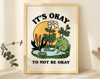 May include: A framed print with a green frog sitting in a pond with a yellow sun and white flower behind it. The text reads "It's okay to not be okay."