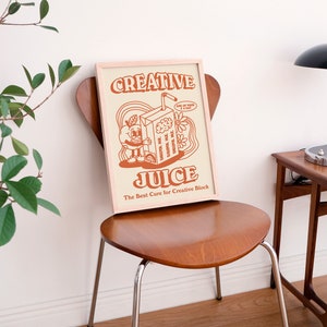 May include: A framed print with a retro illustration of a cartoon character holding a juice box. The text on the print reads "Creative Juice" and "The Best Cure for Creative Block".