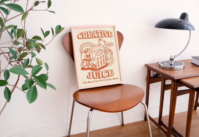 May include: A framed print with a retro illustration of a cartoon character holding a juice box. The text on the print reads "Creative Juice" and "The Best Cure for Creative Block".