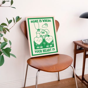 May include: A green and white poster with the text "Home is where your heart is". The poster features a cartoon house with two hearts holding hands in front of it.