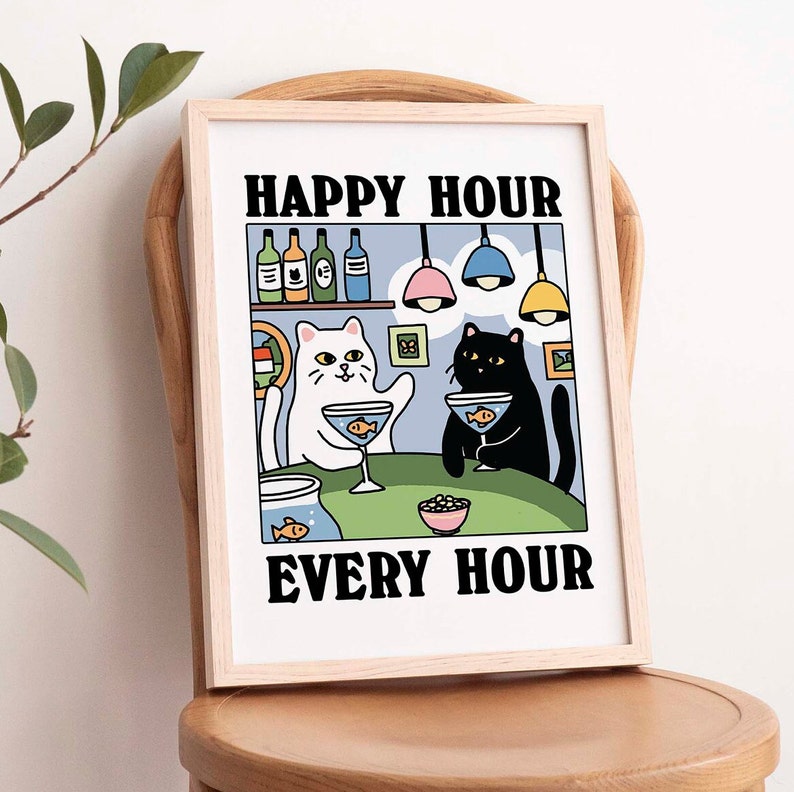 Peut inclure: Une illustration encadr&eacute;e de deux chats dans un bar, l'un blanc et l'autre noir, avec le texte "Happy Hour Every Hour". Les chats tiennent des cocktails avec des poissons &agrave; l'int&eacute;rieur. Il y a des bouteilles d'alcool sur une &eacute;tag&egrave;re derri&egrave;re eux.