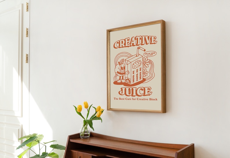 May include: A framed print with a retro-style illustration of a cartoon juice box with a brain inside. The text on the print reads "Creative Juice" and "The Best Cure for Creative Block".