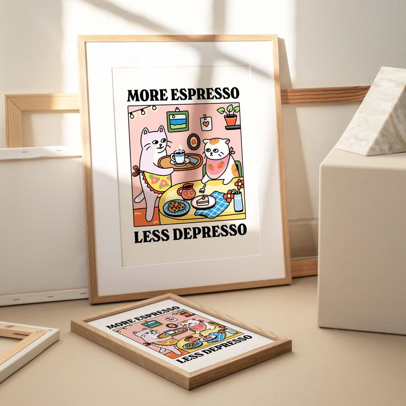 May include: A framed print with a cartoon illustration of two cats sitting at a table with coffee and cake. The text on the print reads "More Espresso Less Depresso".