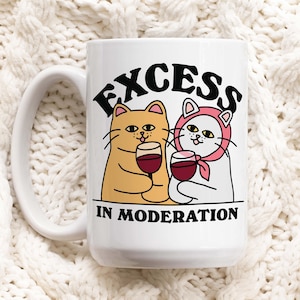 Może przedstawiać: Biały kubek ceramiczny z czarno-białym rysunkiem dwóch kotów pijących wino. Na kubku nadrukowany jest napis "EXCESS IN MODERATION".