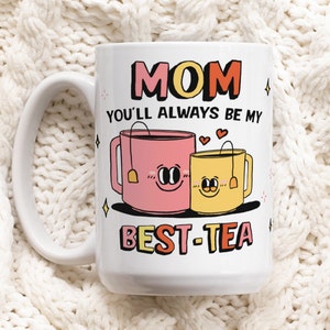 May include: White ceramic mug with a pink and yellow teacup design. The text "MOM YOU'LL ALWAYS BE MY BEST-TEA" is printed on the mug.