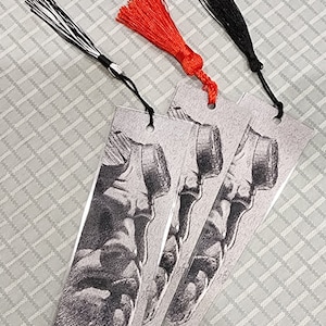 Op de afbeelding: Drie bladwijzers met een zwart-witte tekening van een voet op een transparante achtergrond. Elke bladwijzer heeft een kwast, een zwarte, een rode en een zwart-witte.