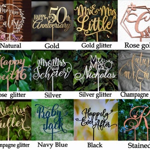 May include: A collection of 10 cake toppers in various colors and styles, including natural wood, gold, silver, rose gold, champagne gold, and black. The toppers feature different designs, such as "Mr. & Mrs. Calise", "Happy 50th Anniversary", "Mr. & Mrs. Little", "Happy Sweet 16", "Mr. & Mrs. Scherer", "Mr. & Mrs. Nicholas", "Future Mr. & Mrs.", "Mr. & Mrs. Fuller", "Baby Jack", and "Happily Ever After".