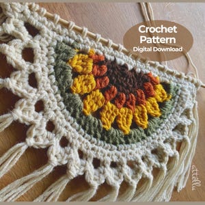 May include: A semi-circular crochet wall hanging featuring a sunflower motif in yellow, orange, and dark brown, surrounded by olive green and cream yarn. The piece is suspended from a wooden dowel and includes cream fringe. Text reads: Crochet Pattern Digital Download.
