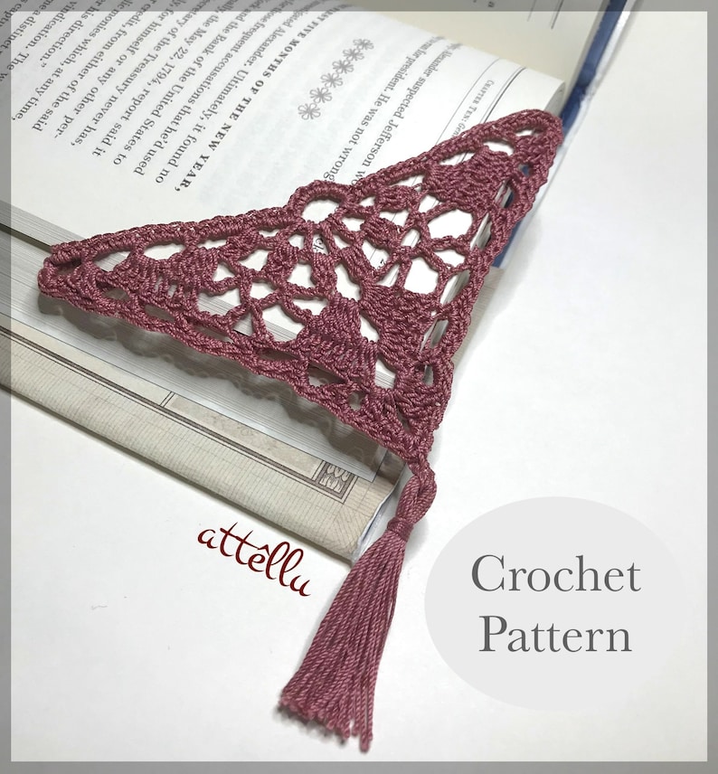 May include: A crocheted bookmark in a dusty rose color with a tassel. The bookmark is in the shape of a triangle with a lacy pattern. The text "att&eacute;llu Crochet Pattern" is visible in the image.