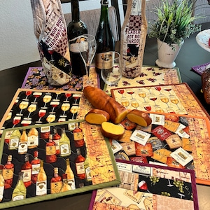 May include: A set of four quilted wine bottle holders and four quilted placemats with a wine theme. The placemats feature a variety of wine bottles, grapes, and wine glasses. The bottle holders are made of fabric and have a quilted design. The bottle holders are decorated with wine-themed fabric scraps and have a variety of colors, including red, white, and green. The placemats are also decorated with wine-themed fabric scraps and have a variety of colors, including red, white, and green.