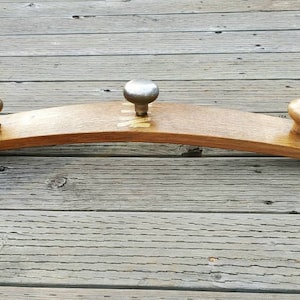 Könnte beinhalten: Ein Holz-Kleiderständer aus einer Weinfassdauble mit drei Metallknöpfen zum Aufhängen von Gegenständen. Der Kleiderständer ist gebogen und hat eine natürliche Holzoptik.