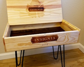 Puede incluir: Una caja de madera de vino reutilizada como una mesa pequeña con patas de horquilla negras. La caja tiene una etiqueta que dice "2014 INSIGNIA".