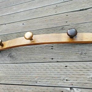 May include: A wooden coat rack made from a reclaimed wine barrel with three metal knobs for hanging items. The knobs are gold, silver, and black.