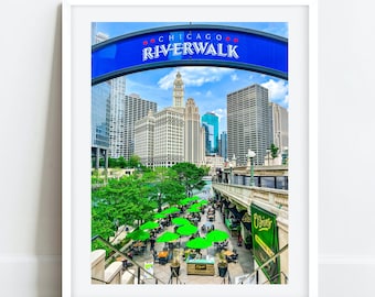 May include: A framed photograph of the Chicago Riverwalk with a blue sign that reads "Chicago Riverwalk" and a view of the city skyline. The photo shows green trees, a river, and people sitting at tables under green umbrellas.