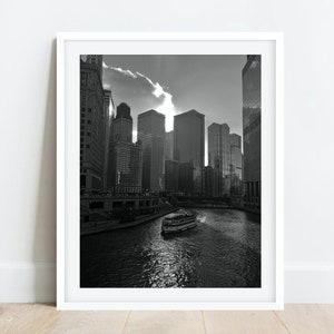 K&ouml;nnte beinhalten: Ein Schwarzwei&szlig;foto einer Skyline mit hohen Geb&auml;uden und einem Fluss im Vordergrund. Ein Boot f&auml;hrt den Fluss entlang.