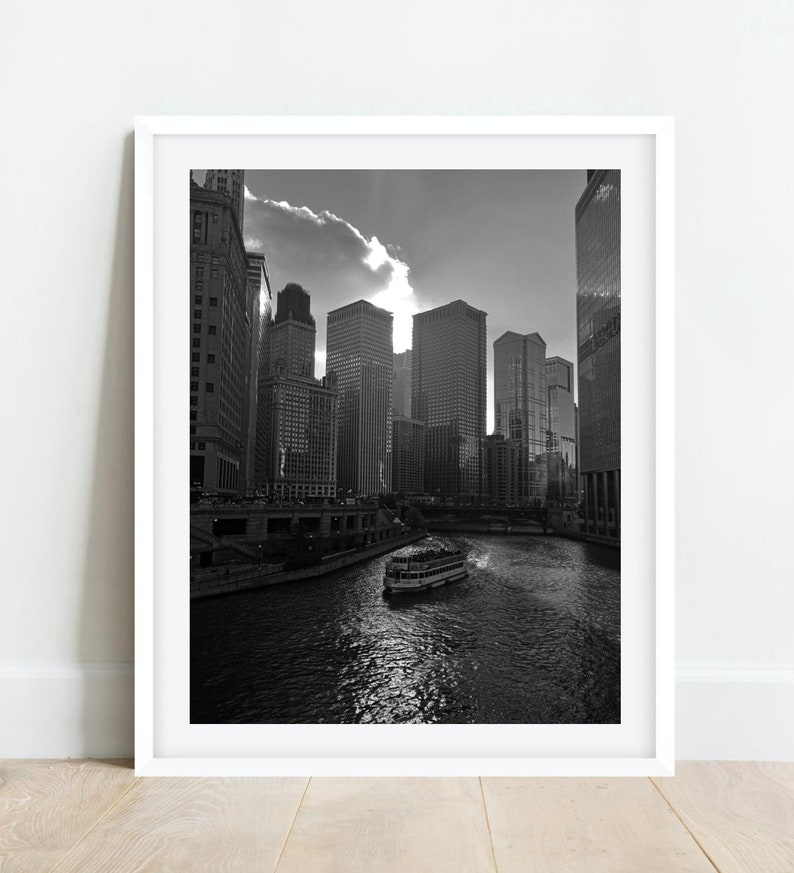 K&ouml;nnte beinhalten: Ein Schwarzwei&szlig;foto einer Skyline mit hohen Geb&auml;uden und einem Fluss im Vordergrund. Ein Boot f&auml;hrt den Fluss entlang.