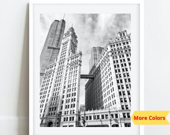 May include: Black and white photograph of a tall building with a clock tower in Chicago. The building is surrounded by other tall buildings. The photo is taken from a low angle, looking up at the building.