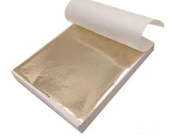 Può includere: Un pacchetto di fogli di oro, ogni foglio è sottile e delicato, e la foglia d'oro è lucida e riflettente. I fogli sono confezionati in una busta di carta bianca.