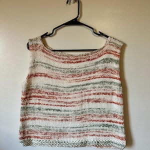 May include: A sleeveless knitted top with a striped pattern in shades of white, orange, and green. The top has a scoop neck and a ribbed hem.