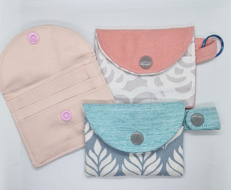 3 credit card wallets, one with keyring, one with snap strap. One is open to show the card slots and the snap closure from the inside.