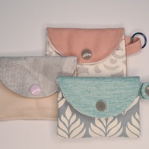 3 mini card wallets, all closed with the snap.Pink one has a keyring, blue one has a strap with the snap and the grey one without any.