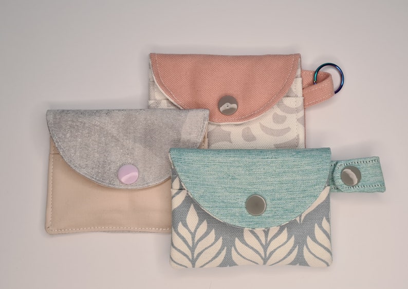 3 mini card wallets, all closed with the snap.Pink one has a keyring, blue one has a strap with the snap and the grey one without any.