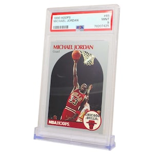 May include: A graded Michael Jordan 1990 NBA Hoops trading card, #65, in a clear plastic case. The card features a photo of Jordan in a red and black Chicago Bulls uniform, shooting a basketball. The card is graded as Mint 9.
