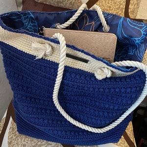 Puede incluir: Un bolso tote azul y crema con asa de cuerda. El bolso tiene un patr&oacute;n de punto texturizado y un interior floral azul. Una cartera beige es visible dentro del bolso.