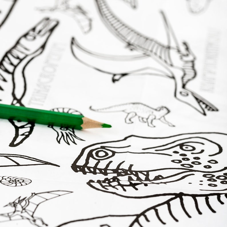 May include: A close-up of a coloring page with a green pencil on top. The page features various dinosaur skeletons, including a T-Rex skull, a Pterodactyl, and a Stegosaurus.