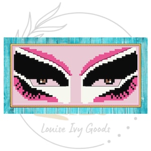 May include: A framed cross-stitch art piece featuring a stylized pair of eyes. The eyes have black eyelashes and eyebrows, with pink and black pixelated details. The frame is a light blue color with a gold inner border. The text "Louise Ivy Goods" is at the bottom.