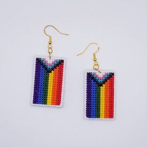 May include: A pair of rainbow pride flag earrings with gold hooks. The earrings are made of colorful beads and are rectangular in shape.
