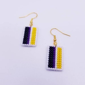 May include: A pair of gold earrings with a white, purple, and yellow striped design. The earrings are rectangular in shape and are made of fabric.