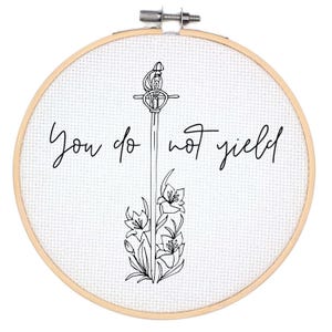 Pode incluir: Um aro de bordado branco com um desenho de linha preta de uma espada com flores e o texto "You do not yield".