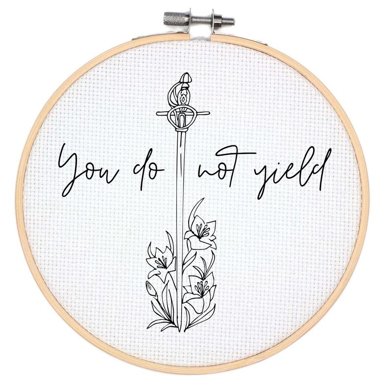 Pode incluir: Um aro de bordado branco com um desenho de linha preta de uma espada com flores e o texto "You do not yield".