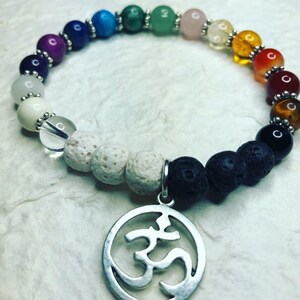 May include: A rainbow chakra bracelet with white lava rock and black lava rock beads. The bracelet has a silver Om charm.