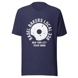 May include: A navy blue t-shirt with a white graphic of a bagel with a bite taken out of it. The graphic says "Bagel Bakers Local 338 New York City Trade Union".