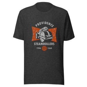Op de afbeelding: Een donker grijs t-shirt met een vintage-stijl afbeelding van een stoomwals. De afbeelding bevat de tekst "Providence Steamrollers 1946-1949" en een rode en witte stervormige uitbarsting.